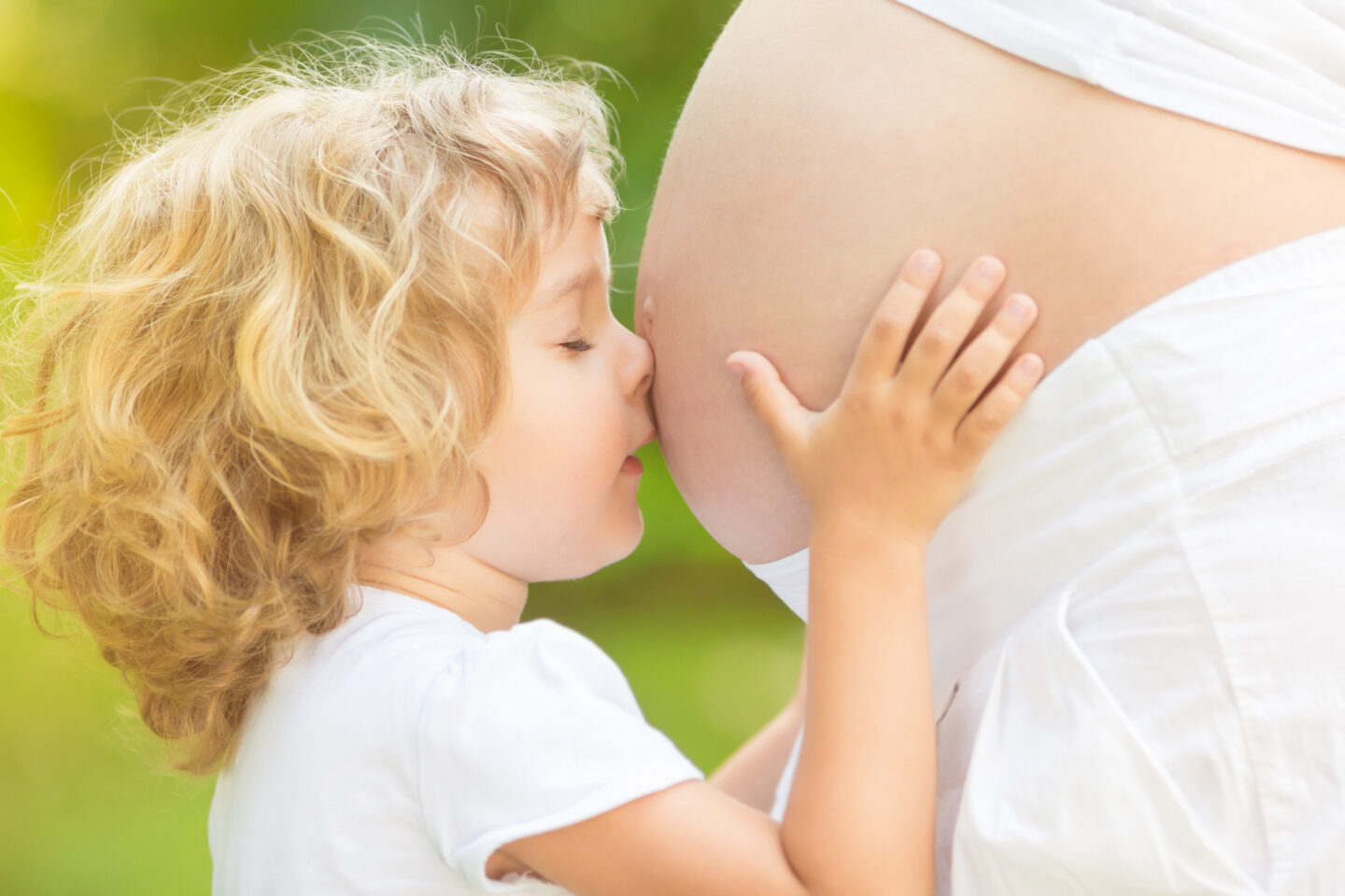 Kind küsst den Bauch der schwangeren Mutter