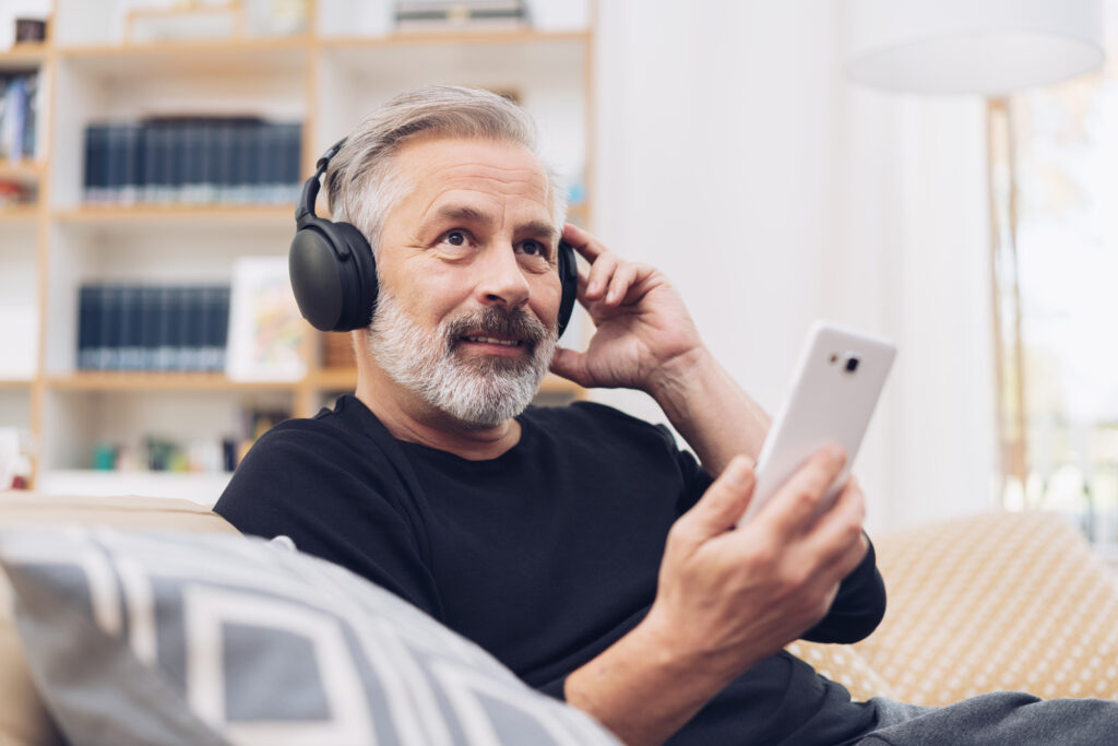 Mann im mittleren Alter hört Podcast mit Kopfhörern im Wohnzimmer