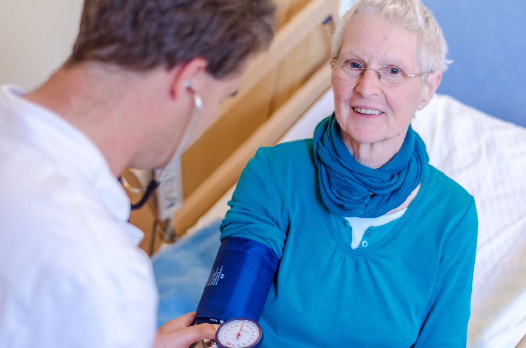 Arzt misst Blutdruck bei einer älteren Dame im Krankenbett