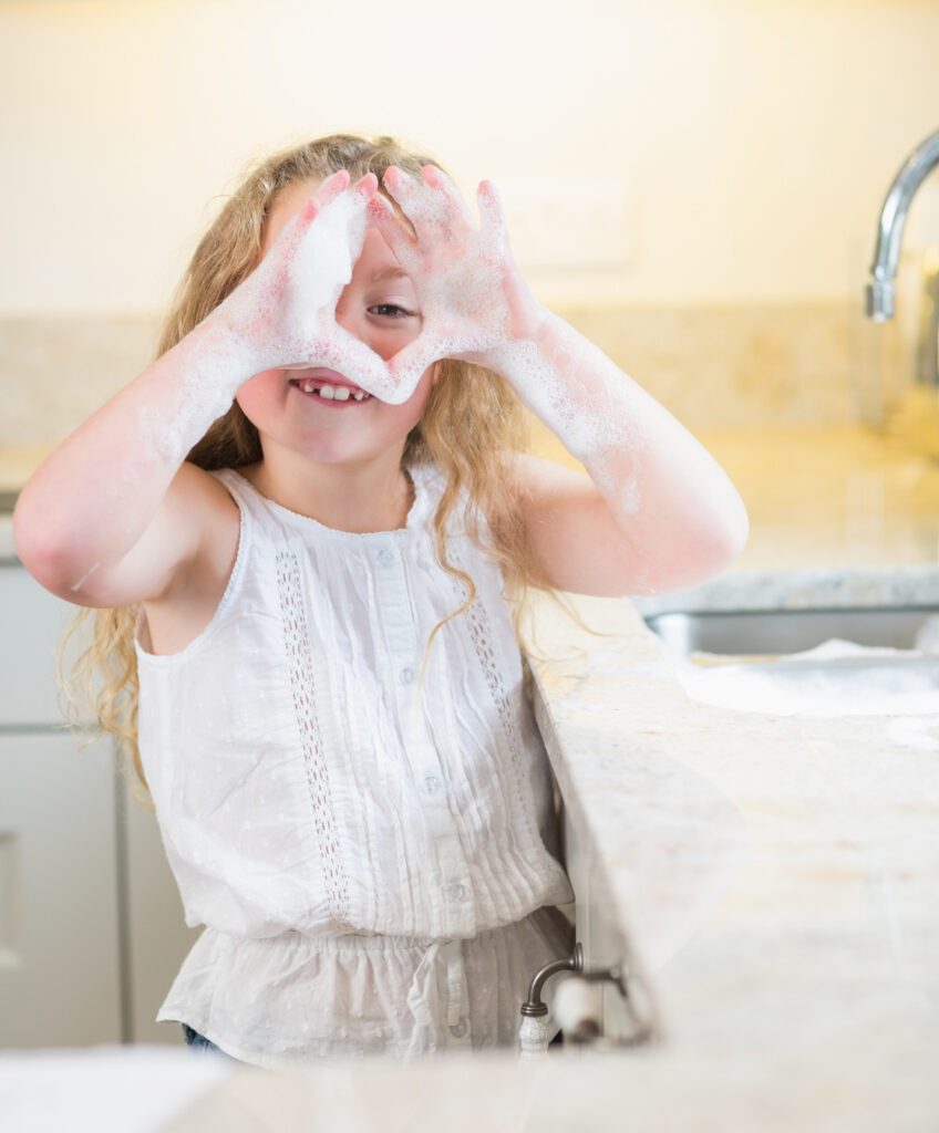 Kind hält sich mit Seife eingeschäumte Hände vor das Gesicht