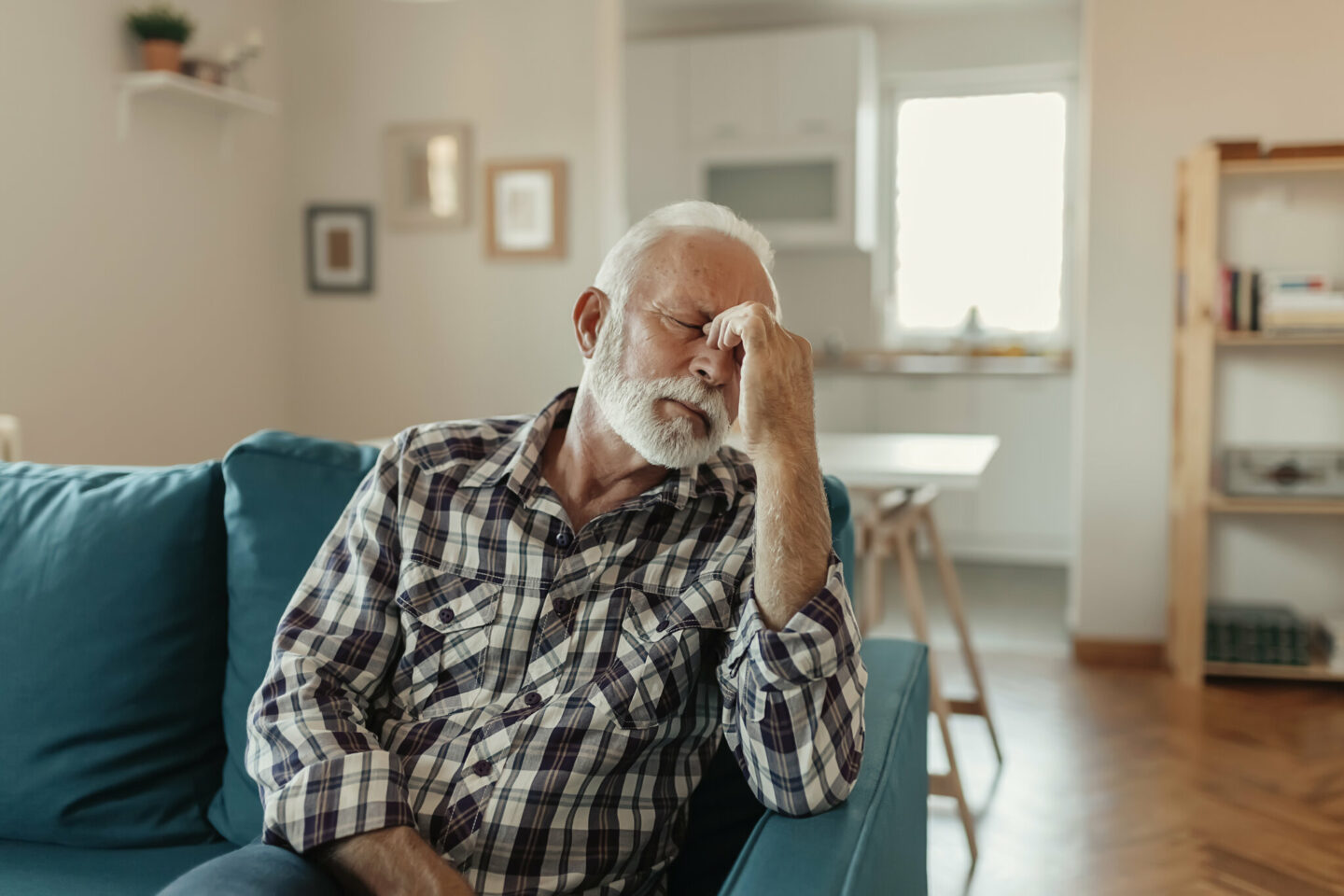 Ein verzweifelter älterer Mann, der an Migräne leidet, während er auf dem Sofa im Wohnzimmer sitzt.