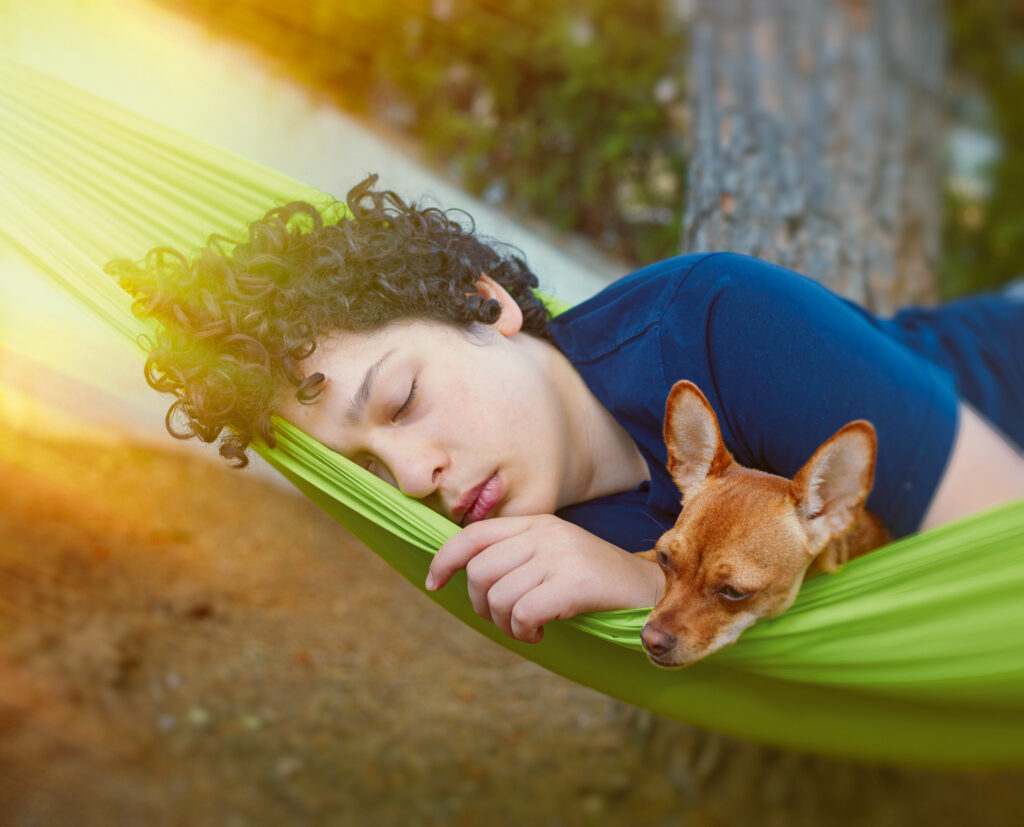 Junger Mann mit Hund liegt schlafend in einer Hängematte unter einem Baum