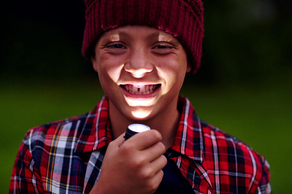Junge im Dunkeln mit einer leuchtenden Taschenlampe vor seinem Gesicht