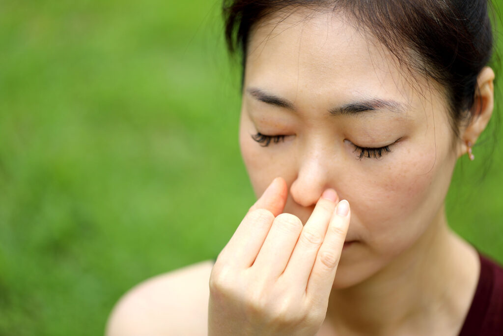 Asiatische Frau im Park hat Probleme mit der Atmung durch die Nase