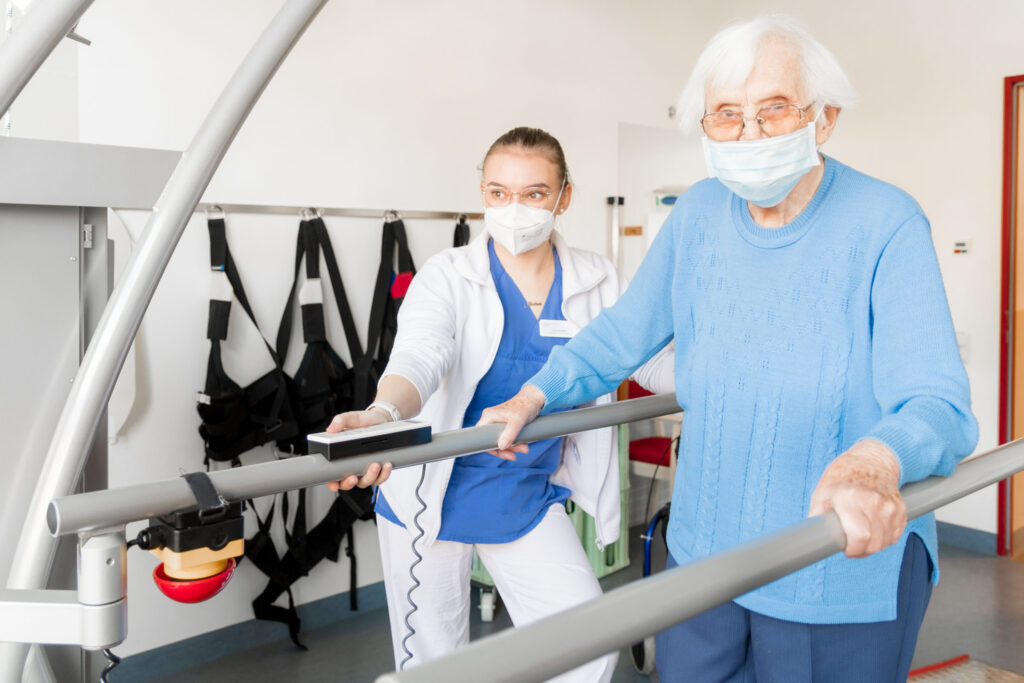 Ältere Schlaganfallpatientin macht nach erfolgter erfolgreicher Behandlung mittels Thrpmbektomie die ersten Rehaschritte an einem Sportgerät im Sana Klinikum Borna