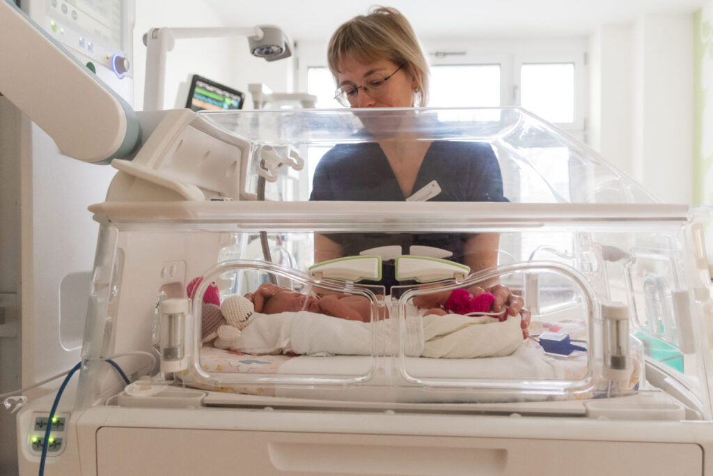 Kinderkrankenschwester steht vor dem Inkubator und überwacht einen neugeborenen Säugling