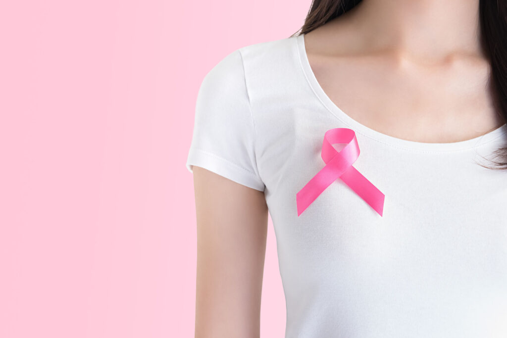 Woman in white t-shirt with satin pink ribbon on her chest, supporting symbol of breast cancer awareness campaign in October