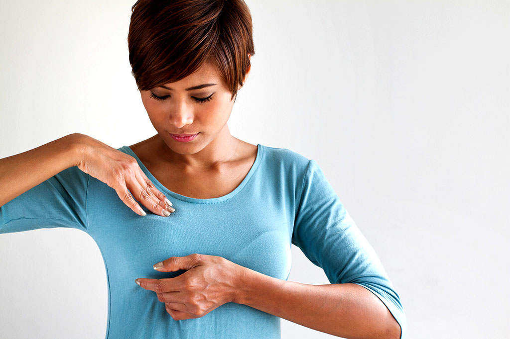 Brustselbstuntersuchung (Symbolbild): Junge Frau in blauem Oberteil tastet Ihre rechte Brust mit beiden Händen nach Knoten bzw. Veränderungen ab