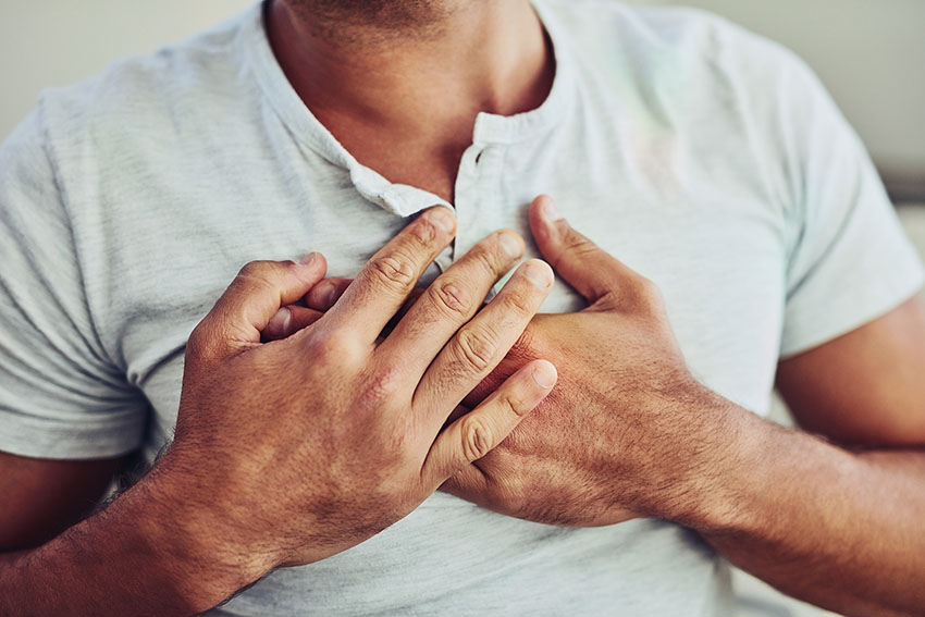 Ein Mann presst beide Hände vor die Brust. Er hat augenscheinlich Brustschmerzen. Detailaufnahme der Brust.