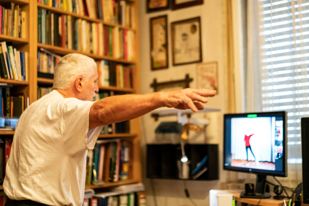 Ein älterer Parkinsonpatient trainiert seine Motorik mittels einer Spielekonsole und eines Bildschirms
